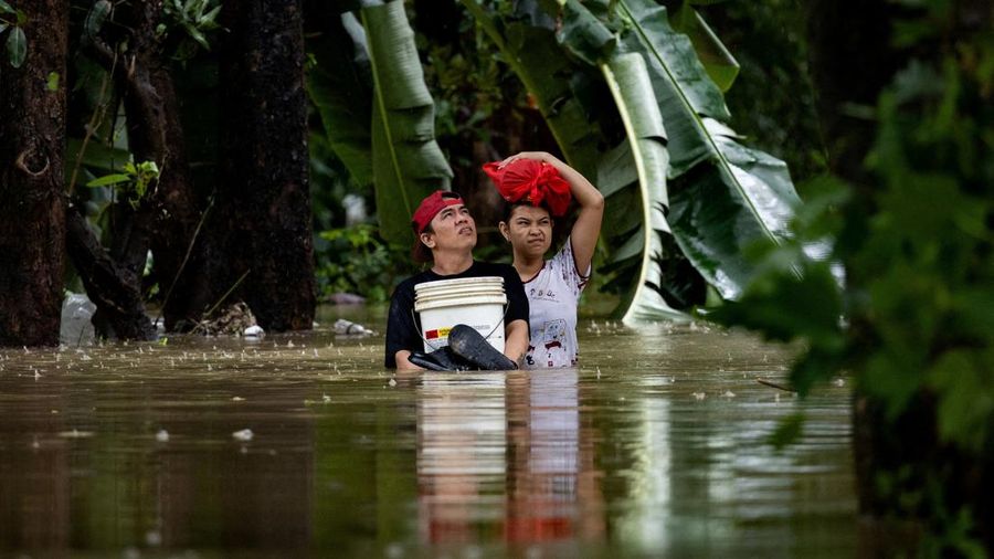 Warga nan membawa barang-barang mereka melangkah menerjang banjir di sebuah desa di tengah hujan monsun barat daya di Bagong Silangan, Quezon City, Filipina, pada 10 Agustus 2026. (REUTERS/Eloisa Lopez)