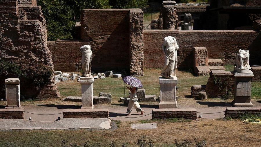 Seorang wanita menggunakan payung untuk berlindung dari terik mentari saat mengunjungi Forum Romawi di tengah suhu nan mendekati 40 derajat Celsius akibat gelombang panas, di Roma, Italia, pada 11 Agustus 2026. (REUTERS/Guglielmo Mangiapane)