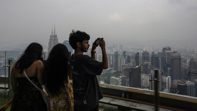 Visitors take pictures from the KL Tower as the Petronas Twin Towers and commercial buildings are covered in haze in Kuala Lumpur on August 11, 2026, as authorities in Malaysia warned of high levels of air pollution from regional wildfires. The Malay