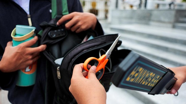 A student prefect holds a pair of scissors, which is used for workshop classes, while using a metal detector and checking students' bags to screen for weapons, as they enter a school in Bangkok, following a deadly shooting at Debsirin Nonthaburi Scho