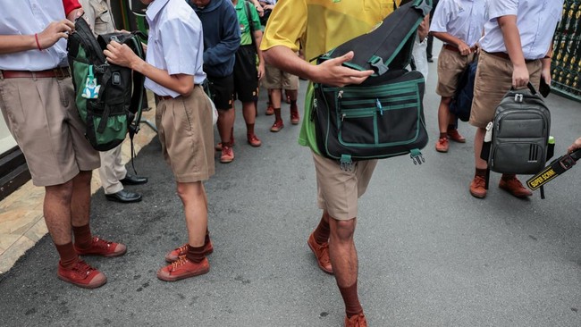 A teacher uses a metal detector to screen for weapons while a student prefect checks students' bags as they enter a school in Bangkok, following a deadly shooting at Debsirin Nonthaburi School in Nonthaburi province on the outskirts of Bangkok, Thail