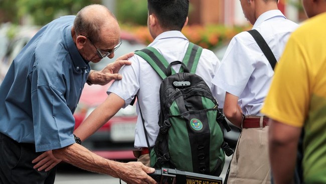 A teacher uses a metal detector to screen for weapons and checks students' bags as they enter a school in Bangkok, following a deadly shooting at Debsirin Nonthaburi School in Nonthaburi province, on the outskirts of Bangkok, Thailand, August 10, 202