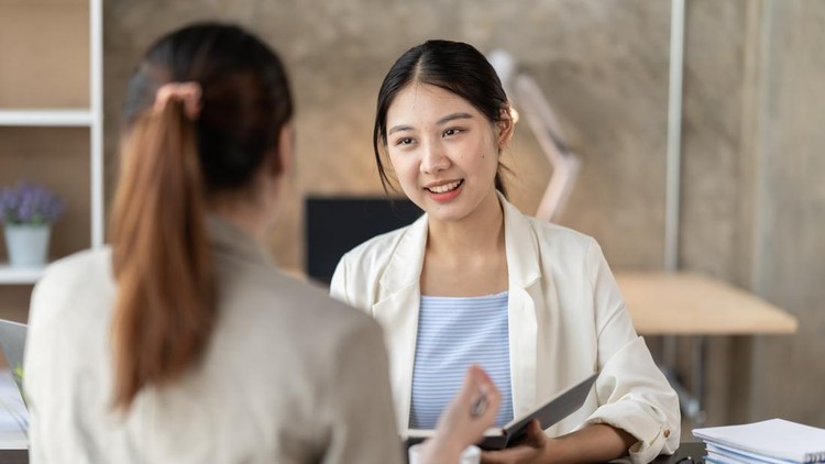 Young beautiful asian business woman is talking to her colleague&comma; while sitting at the desk in a modern office&period; Concept of business success&period;