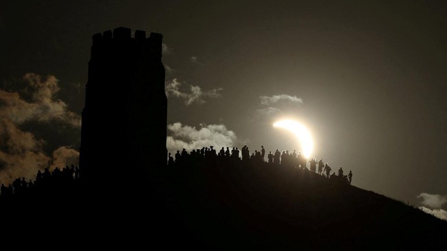 People view a partial solar eclipse beside St Michaels Tower on Glastonbury Tor, in Glastonbury, Britain, August 12, 2026. REUTERS/Toby Melville