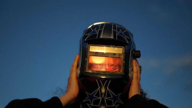 A woman looks at the sun through the welders mask during partial solar eclipse, at the Copernicus Science Centre in Warsaw, Poland, August 12, 2026. REUTERS/Kacper Pempel