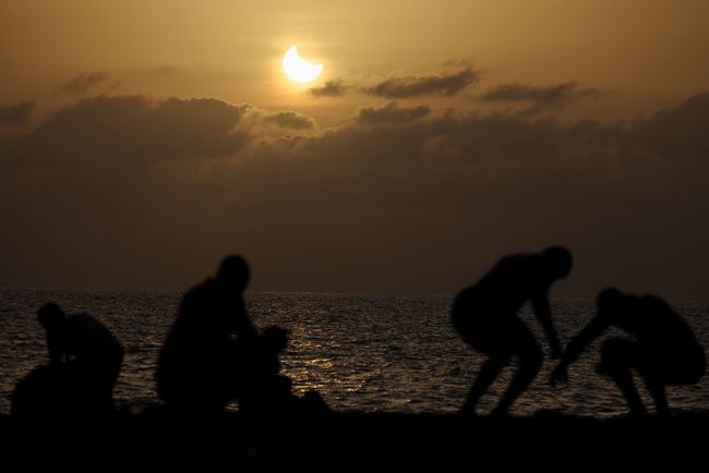 Warga berolahraga di sepanjang pantai saat bulan menutupi sebagian matahari dalam peristiwa gerhana matahari sebagian di Dakar, Senegal, pada 12 Agustus 2026.