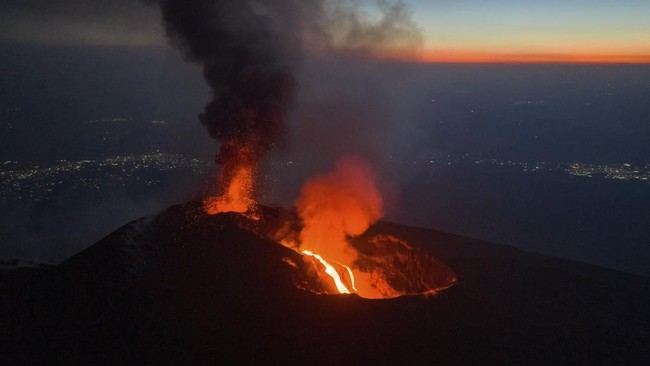 A drone view shows lava flowing from a crater and volcanic fumes rising during an eruption of Mount Etna, with lights from nearby communities visible in the distance, in Sicily, Italy, August 13, 2026. REUTERS/Giuseppe Di Stefano