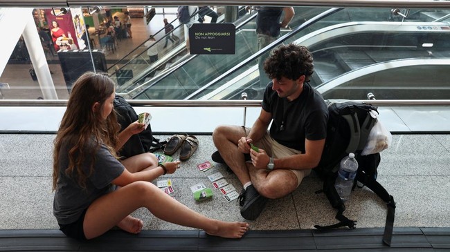 Passengers play a card game as they wait inside the terminal at Vincenzo Bellini Catania Airport following the closure of the airport due to an ash cloud from Sicilys Mount Etna eruption in Catania, Italy, August 14, 2026. REUTERS/Matteo Minnella