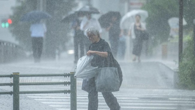 People walk along a street in heavy rain in Tokyo on July 24, 2026. (Photo by Yuichi YAMAZAKI / AFP)