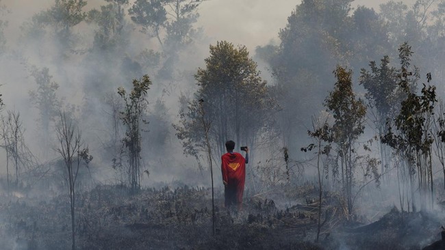 Rudiyansah, 16, wears a Superman costume inspects a fire at a wildfire-affected area in Palangka Raya, Central Kalimantan province, Indonesia, August 14, 2026. REUTERS/Ajeng Dinar Ulfiana