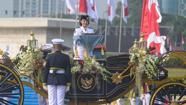 Purna Paskibraka Duta Pancasila 2025 Aliah Sakira (kiri) membawa naskah Proklamasi di atas kereta kencana Garuda Prabayaksa dari Monumen Nasional menuju Istana Merdeka dalam kirab Merah Putih di Jakarta, Senin (17/8/2026). Kirab menuju Istana Merdeka