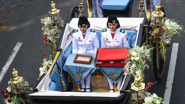 Purna Paskibraka Duta Pancasila 2025 Bianca Sultana Najwa (kanan) dan Aliah Sakira (kiri) membawa bendera pusaka dan naskah Proklamasi di atas kereta kencana Garuda Prabayaksa dari Monumen Nasional menuju Istana Merdeka dalam Kirab Merah Putih di Jak