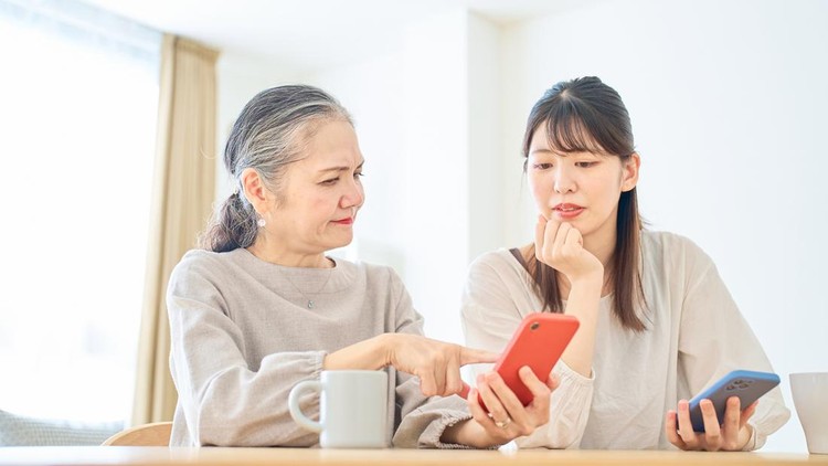 A senior woman and a young woman looking anxiously at their smartphone screens indoors