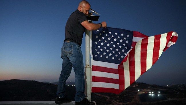 Palestinian-American Loui Ridi, whose home in the Israeli-occupied West Bank has been encircled by militant settlers for more than a week, hangs a U.S. flag after gaining access to his besieged home, in Qusra, Israeli-occupied West Bank, August 17, 2