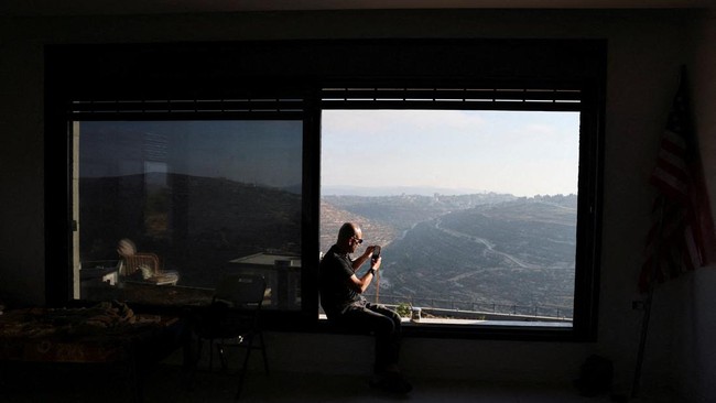 Palestinian-American Loui Ridi takes a picture from a window of his home, which has been encircled by militant settlers for more than a week, after gaining access to it, in Qusra, Israeli-occupied West Bank, August 18, 2026. REUTERS/Ammar Awad REFILE