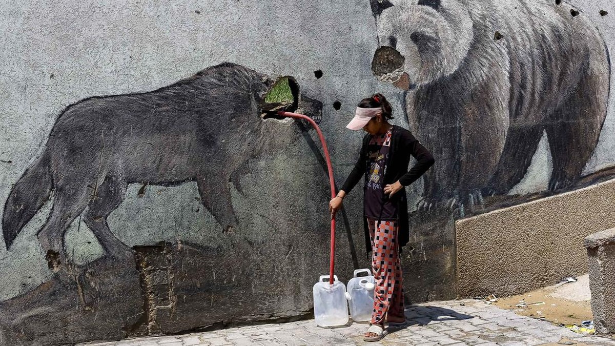 A Palestinian girl fills water containers outside the wall of a zoo damaged during the war, in Gaza City, August 15, 2026. REUTERS/Mahmoud Issa     TPX IMAGES OF THE DAY