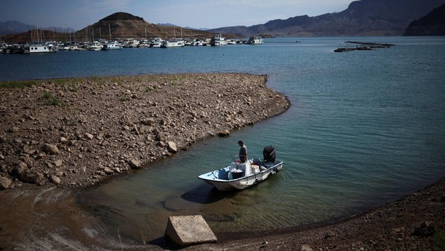 A man wades his boat into the receding shoreline of Lake Mead, the largest reservoir in the United States by water capacity, highlighting the long-term effects of drought and water demand on the Colorado River system, near Boulder City, Nevada, U.S.,