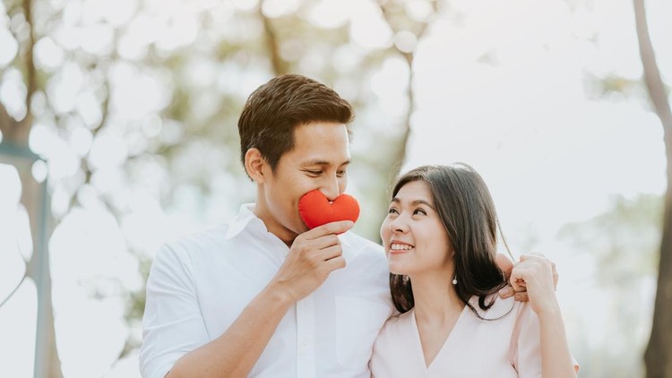 Happy Asian couple in love embracing playing with heart in hand at the park