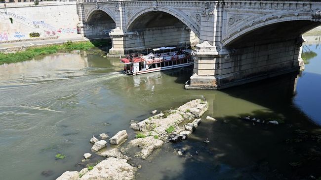 A tourist boat passes near an Ancient Roman bridge emerging from the Tiber River in central Rome on 13 August, 2026. The unusually low waters of the Tiber River have revealed the remains of an ancient Roman bridge believed to date back to the reign o