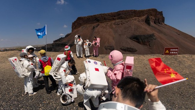 A group of people wearing astronaut costumes gather at Volcano No. 6 of the Wulanhada Volcano Geopark in Ulanqab, Inner Mongolia Autonomous Region, China, July 26, 2026. In China's northern region of Inner Mongolia, black volcanic rock formations hav