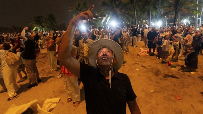 A man films with his smartphone from Qishui Bay Beach during a launch from the Wenchang Space Launch Site in Wenchang, Hainan province, China, August 10, 2026. On a sweltering August night, thousands on China's Hainan island thronged the beaches arou