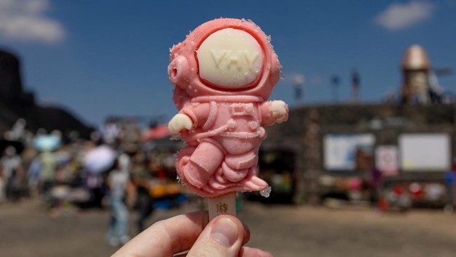 A Reuters photographer holds an ice cream depicting an astronaut, with a full-scale spacecraft lander model in the background, at Volcano No. 6 of the Wulanhada Volcano Geopark, in Ulanqab, Inner Mongolia Autonomous Region, China, July 26, 2026. In C