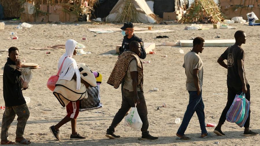 Para migran dikawal dari kamp darurat di pantai menuju tempat penampungan resmi di beragam letak di kota tersebut setelah pihak berkuasa membersihkan area itu—menyusul penyeberangan massal dari Maroko—di wilayah kantong Spanyol di Afrika Utara, Ceuta, pada 20 Agustus 2026.