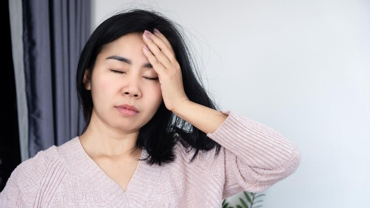 Asian woman suffering from a painful headache&comma; migraine&comma; or vertigo&comma; touching her forehead with eyes closed in discomfort&comma; concept of stress&comma; fatigue&comma; illness&comma; and chronic pain at home indoors