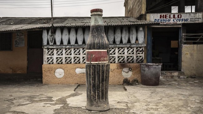 A Coca-Cola bottle-shaped coffin, designed in reference to the deceased's fondness for the soft drink, is pictured outside the Hello Design Coffin workshop in Accra, on August 17, 2026. Fantasy coffins are a distinctive Ghanaian funerary tradition, p