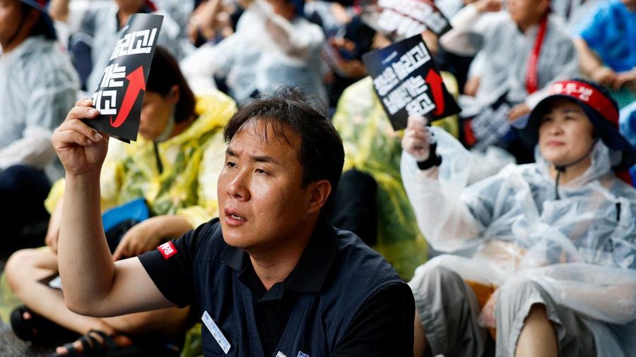 Seorang personil Serikat Pekerja Logam Korea memegang plakat nan menuntut perpanjangan usia pensiun dan kenaikan nilai pasokan komponen dalam sebuah unjuk rasa di luar instansi pusat Hyundai Motor Company, saat serikat pekerja perusahaan otomotif tersebut menggelar pemogokan kerja total pertama dalam satu dasawarsa terakhir, di Seoul, Korea Selatan, pada 21 Agustus 2026.