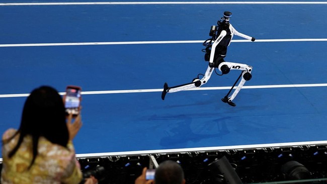 Spectators use smartphones as they watch a Tiangong humanoid robot compete during a 400m large-sized group preliminary race, following the opening ceremony of the 2026 World Humanoid Robot Games, at the National Speed Skating Oval, in Beijing, China