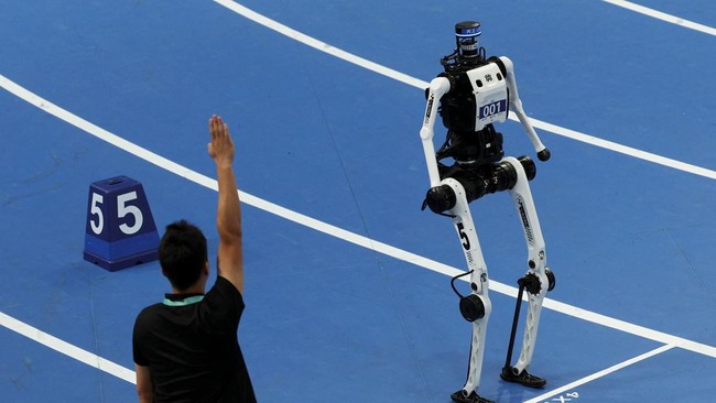 A referee gestures next to a Tiangong Ultra humanoid robot at the start of a 400m large-size group preliminary race, during the second World Humanoid Robot Games at the National Speed Skating Oval in Beijing, China August 22, 2026. REUTERS/Florence L