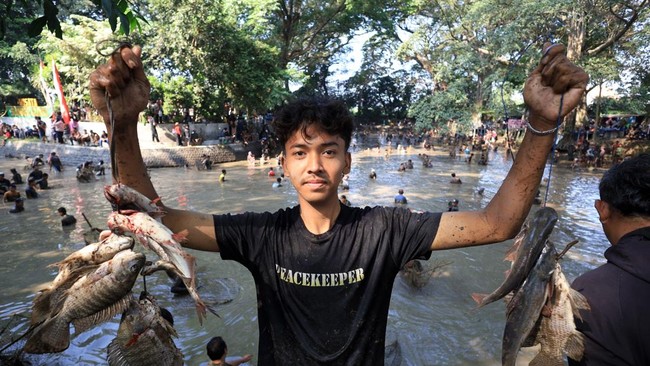 Warga mengangkat ikan hasil tangkapan saat tradisi Grobyak Ikan di Sumber Gundi, Kabupaten Kediri, Jawa Timur, Minggu (23/8/2026). Tradisi memanen ikan hanya sekali dalam setahun tersebut merupakan cara warga sekitar mensyukuri aliran mata air yang t