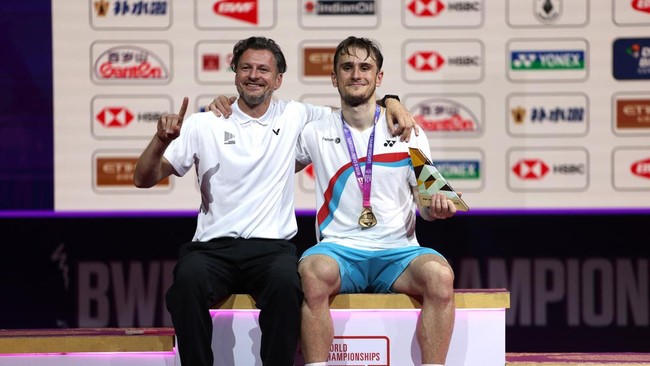 Badminton - BWF World Championships - Indira Gandhi Indoor Stadium, New Delhi, India - August 23, 2026 France's Alex Lanier poses with his trophy and medal alongside coach Kestutis Navickas after winning his men's final against Japan's Kodai Naraoka