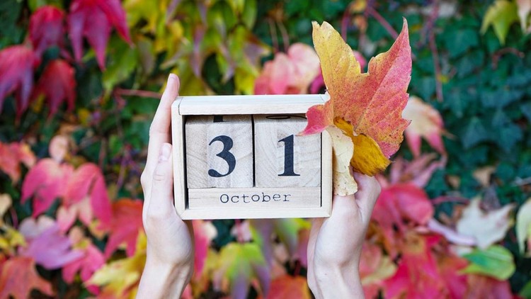 Wooden calendar in the hands of a young woman&comma; the date is October 31&comma; against the background of autumn leaves&period;