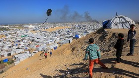 Boys fly a kite against the backdrop of smoke rising from the Gath shelter, that houses displaced Palestinians, after an Israeli air strike in the west of Khan Yunis, southern Gaza Strip on January 31, 2026. Israeli air strikes killed 11 people in th