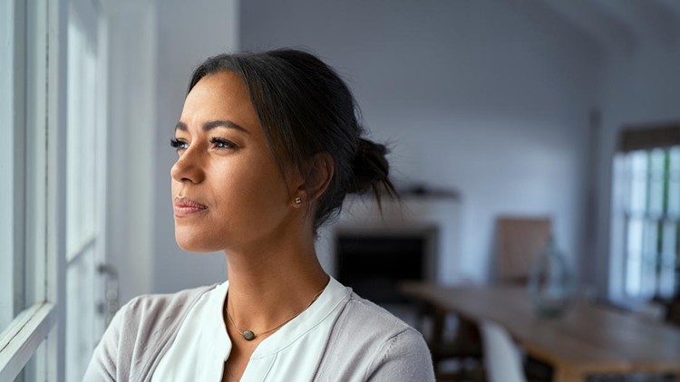 Mature african woman looking outside window with uncertainty&period; Thoughtful mid adult woman looking away through the window while thinking about her future business after pandemic&period; Close up face of doubtful lady at home with pensive expression and copy space&period;