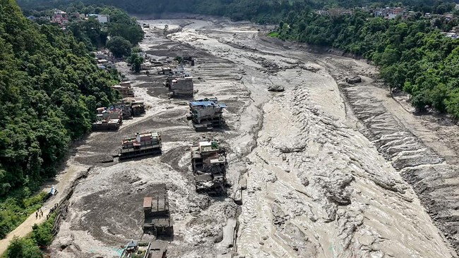 Houses lie partially submerged in muddy water along a riverside after flash floods at Trishuli Bazar in Nepal's Nuwakot district on August 26, 2026. A massive flood swept through Nepal's northern Rasuwa district on August 26, damaging roads and power