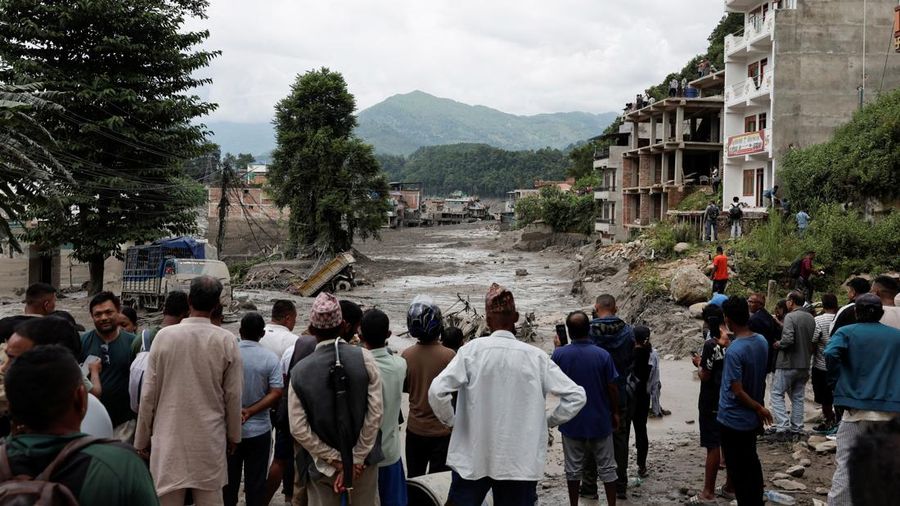 Warga berdiri di dekat rumah-rumah nan tertutup lumpur dan sebuah jalan setelah banjir bandang di Trishuli, Distrik Nuwakot, Nepal, pada 26 Agustus 2026. (REUTERS/Navesh Chitrakar)