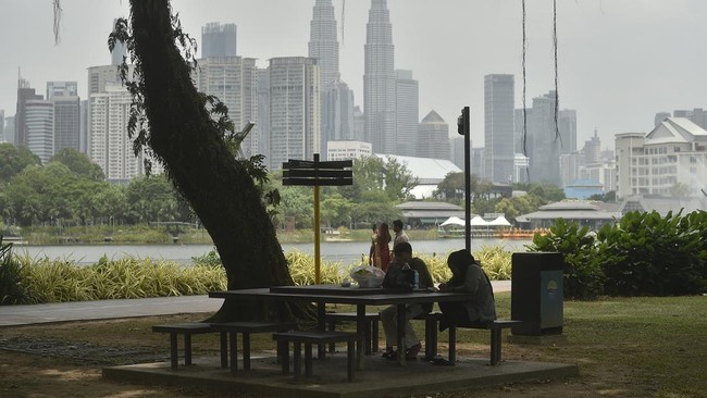 Parkgoers sit by a lake as the landmark Petronas Twin Towers (C) is obscured by haze in Kuala Lumpur on August 26, 2026, amid high levels of air pollution from regional wildfires. Indonesia has for weeks battled wildfires that have led to school clos