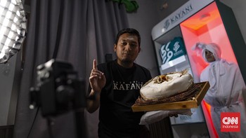 Di sebuah bangunan di kota Bandung, Yoka Brahma Putra menjual kain kafan sambil berseru checkout sebelum meninggal, ditemani sosok berbalut kain kafan mirip pocong yang berdiri diam di belakangnya, dan siaran itu viral. (CNN Indonesia/ Adhi Wicaksono