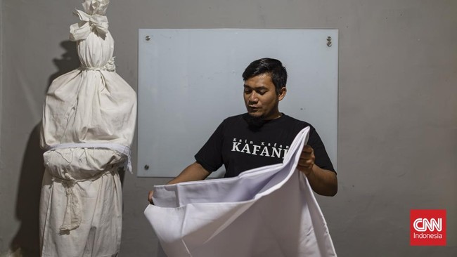 Di sebuah bangunan di kota Bandung, Yoka Brahma Putra menjual kain kafan sambil berseru checkout sebelum meninggal, ditemani sosok berbalut kain kafan mirip pocong yang berdiri diam di belakangnya, dan siaran itu viral. (CNN Indonesia/ Adhi Wicaksono