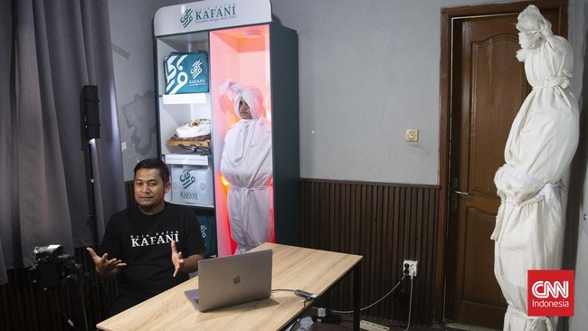 Di sebuah bangunan di kota Bandung, Yoka Brahma Putra menjual kain kafan sambil berseru checkout sebelum meninggal, ditemani sosok berbalut kain kafan mirip pocong yang berdiri diam di belakangnya, dan siaran itu viral. (CNN Indonesia/ Adhi Wicaksono