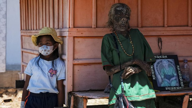 A girl stands next to the remains of her great-grandmother Sara Taba, after they were removed from the burial chamber during Ma'nene, a Torajan ritual where families exhume, clean and redress their deceased relatives to honour them, in Pangala, North