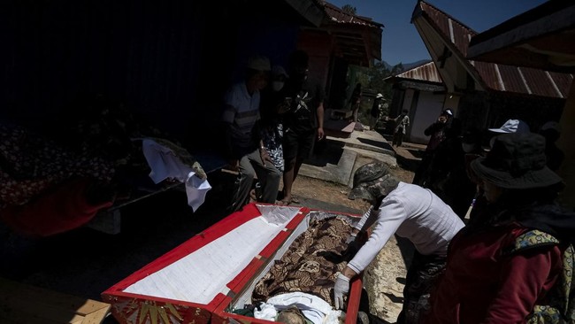 Relatives stand near the remains of their family after they were removed from the burial chamber during Ma'nene, a Torajan ritual where families exhume, clean and redress their deceased relatives to honour them, in Pangala, North Toraja, South Sulawe