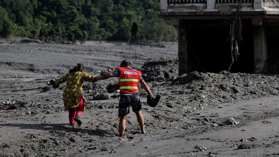 Seorang petugas penyelamat membantu seorang wanita melintasi jalan berlumpur setelah banjir bandang dan tanah longsor di Trishuli, distrik Nuwakot, Nepal, pada 28 Agustus 2026.