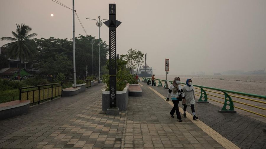 Warga nan mengenakan masker pelindung melangkah di tepi Sungai Kapuas saat kabut asap akibat kebakaran rimba menyelimuti area tersebut di Pontianak, Provinsi Kalimantan Barat, Indonesia, pada 27 Agustus 2026.