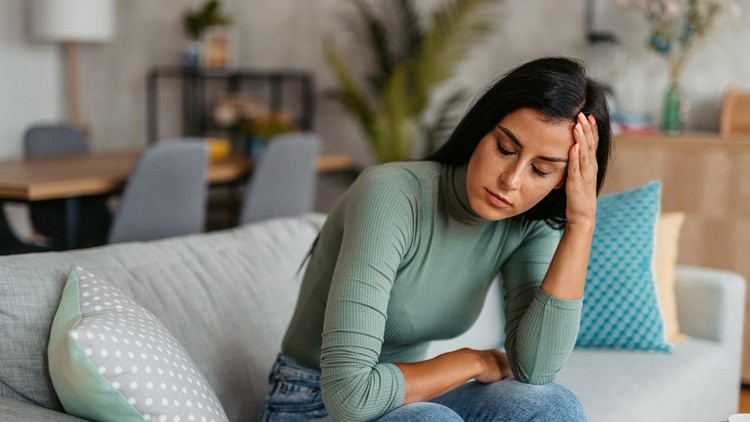 Young woman having a headache while sitting on the sofa at home&period;