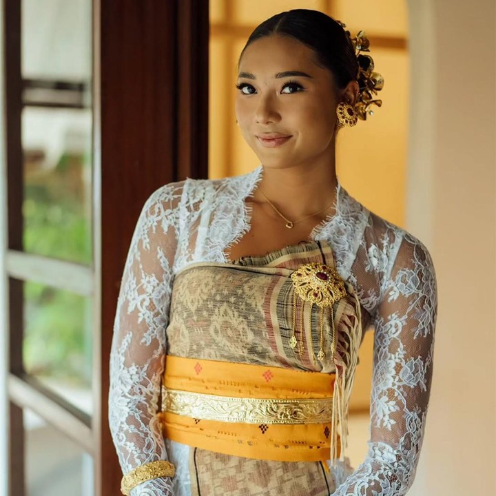 <p>Suri sendiri tampil anggun mengenakan kebaya putih yang ditutupi kain songket Bali berwarna cokelat. Suri terlihat menata rambutnya dengan model sanggul dan menambahkan aksesori semanggi kamboja Bali berwarna emas. (Foto: Instagram @lunamaya)</p>
