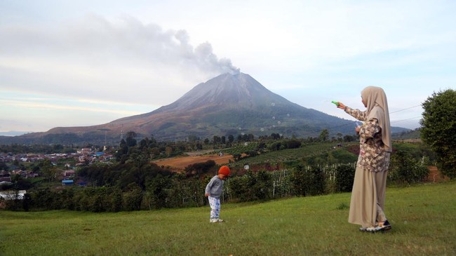 Wisatawan bermain bersama anaknya saat erupsi Gunung Sinabung di Desa Kutarayat, Kecamatan Naman Teran, Kabupaten Karo, Sumatera Utara, Selasa (1/9/2026). Pusat Vulcanologi dan Mitigasi Bencana Geologi menyampaikan bahwa tingkat aktivitas Gunung Sina
